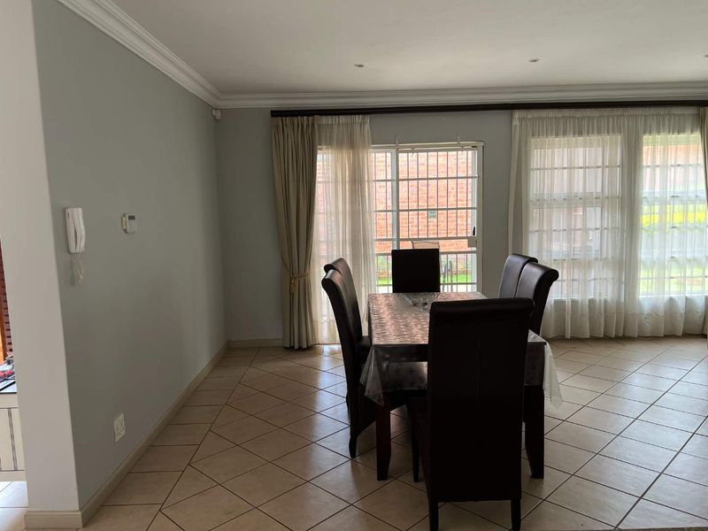 A bright dining area featuring tiled flooring, decorative cornicing, and a sliding glass door with security gate providing access to the exterior.