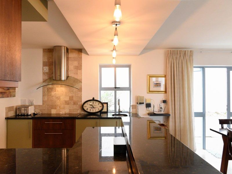 Modern kitchen featuring dark granite countertops, stainless steel extractor fan, tiled splashback, and elegant pendant lighting over a breakfast bar area.