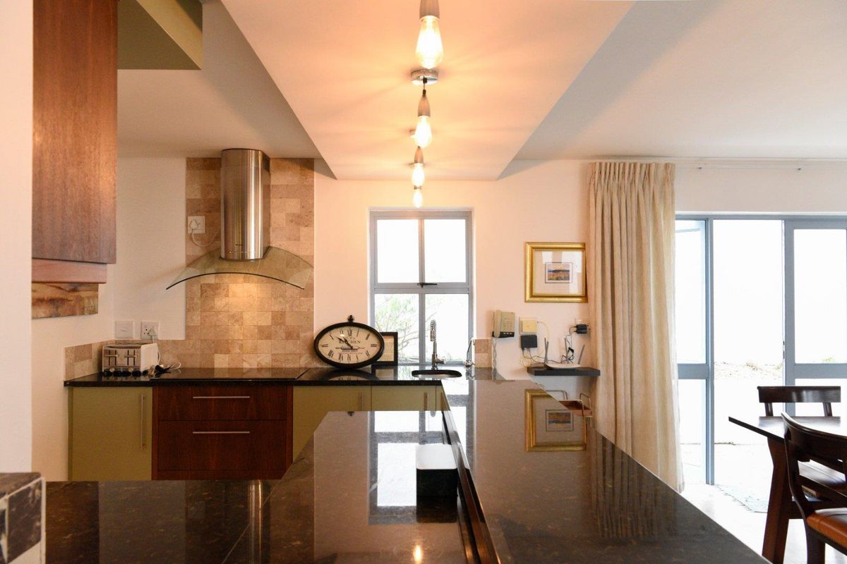 Modern kitchen featuring dark granite countertops, stainless steel extractor fan, tiled splashback, and elegant pendant lighting over a breakfast bar area.