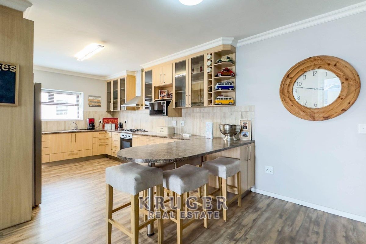 A functional kitchen featuring light wood cabinetry, stone-look countertops, a breakfast bar, and integrated appliances, finished with modern laminate flooring.