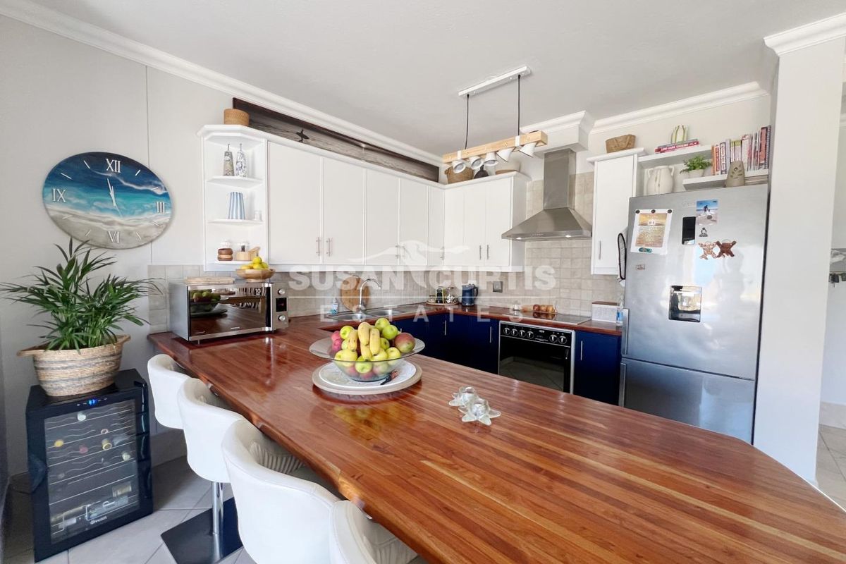 A well-appointed kitchen featuring white upper cabinetry, dark lower cabinets, a wooden breakfast bar, stainless steel extractor fan, and tiled flooring.
