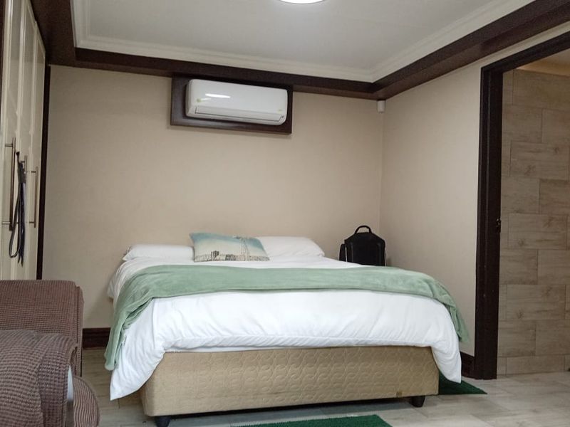 A well-maintained bedroom featuring built-in cupboards, an air conditioning unit, and tiled flooring, with an adjoining bathroom entrance.