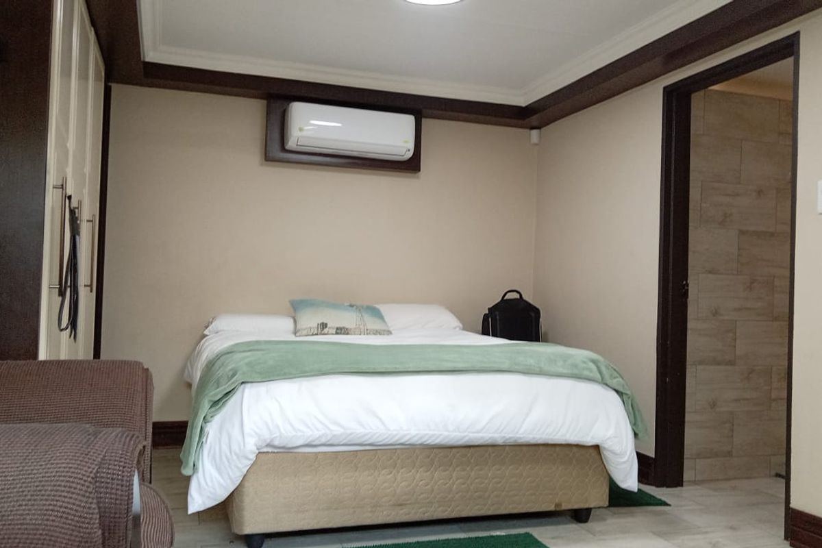 A well-maintained bedroom featuring built-in cupboards, an air conditioning unit, and tiled flooring, with an adjoining bathroom entrance.