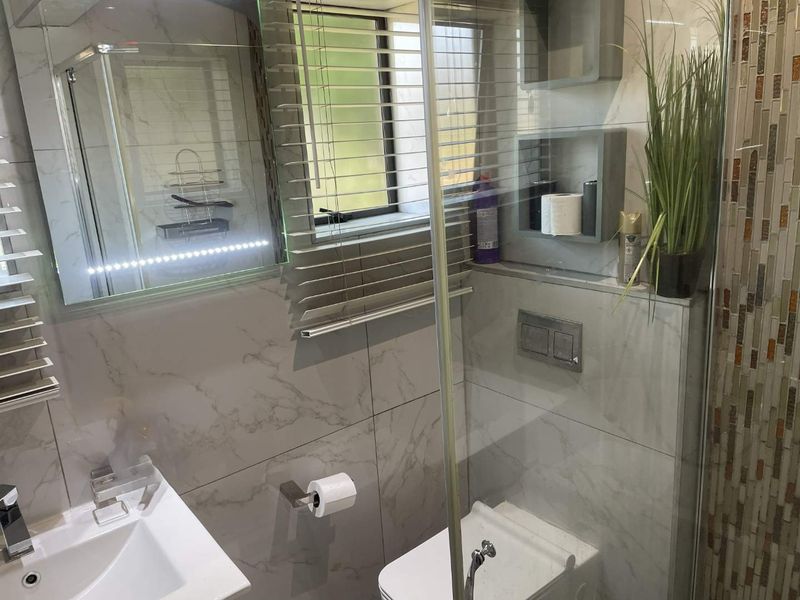 Modern bathroom featuring marble-effect wall tiles, a wall-mounted toilet, glass shower screen, and a contemporary vanity with an integrated LED mirror.