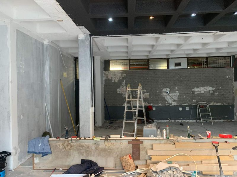 An open-plan retail space currently undergoing renovation, featuring a distinctive coffered ceiling, exposed brickwork, and raw concrete elements ready for final finishes.