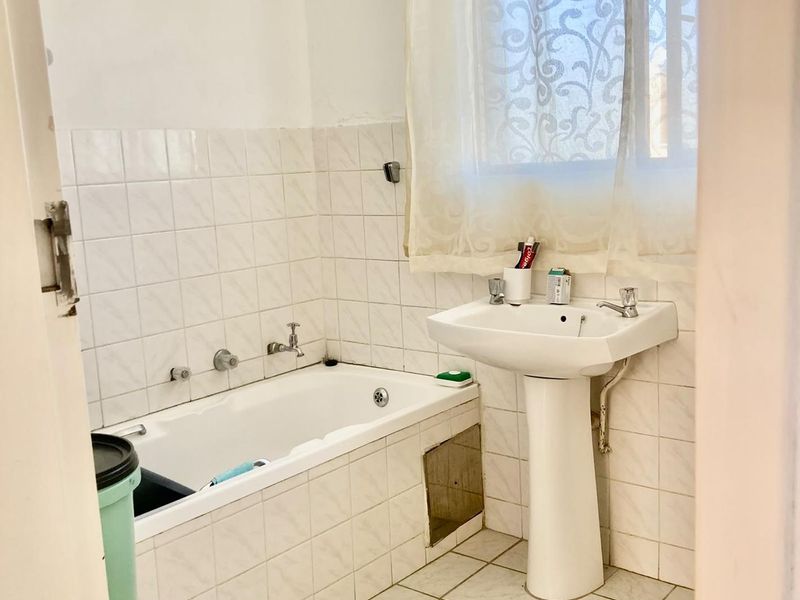 A dated bathroom featuring a pedestal washbasin and a built-in bathtub with wall-to-wall tiling, requiring cosmetic updates to modernize the space.