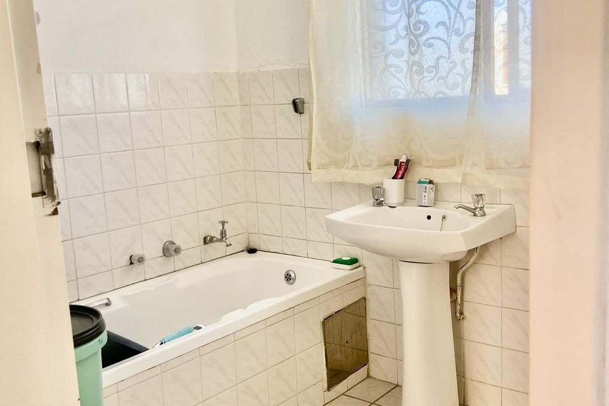 A dated bathroom featuring a pedestal washbasin and a built-in bathtub with wall-to-wall tiling, requiring cosmetic updates to modernize the space.