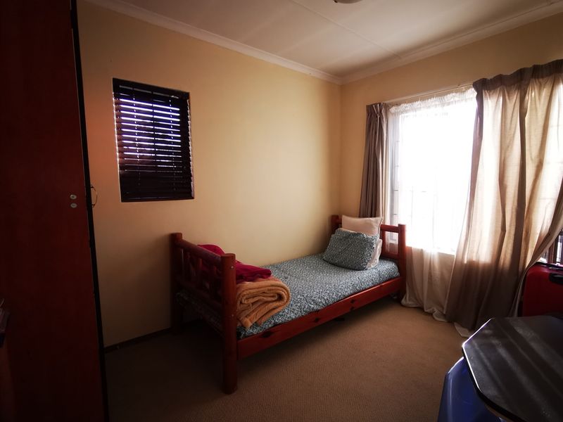 A functional bedroom featuring carpeted flooring, a built-in cupboard, and natural light from dual windows.