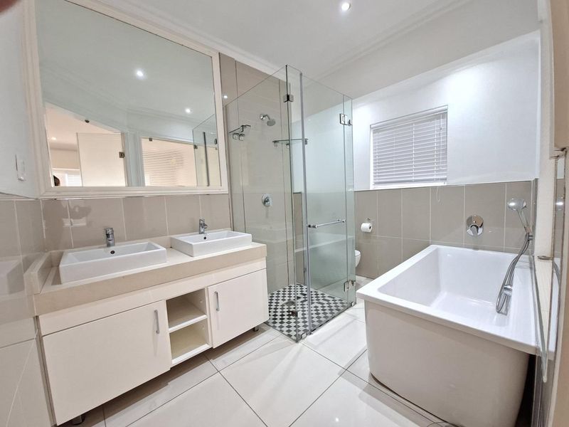 Modern bathroom featuring a double vanity, glass-enclosed shower, and a sleek freestanding bathtub with contemporary fixtures and neutral tiling.