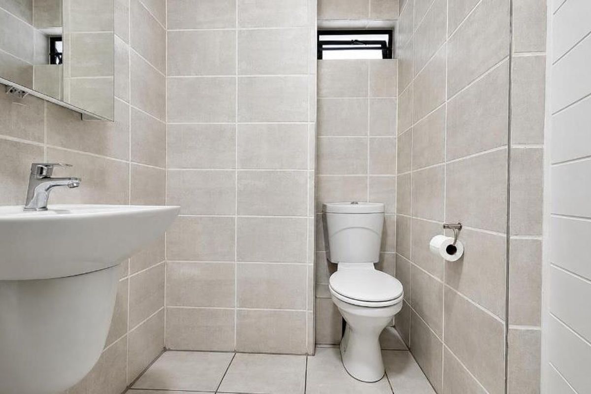 A clean, modern bathroom featuring neutral wall and floor tiles, a wall-mounted basin, and a standard toilet.