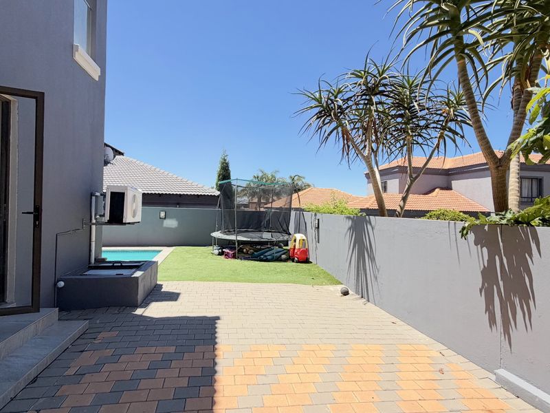 Rear exterior view featuring a paved patio area, artificial lawn, and a swimming pool enclosed by a boundary wall.