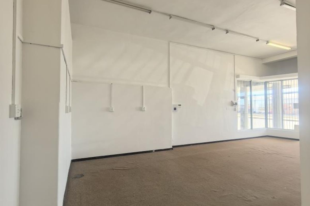 An empty, open-plan office space featuring large windows, fluorescent lighting, and worn carpeting, suitable for a variety of business configurations.