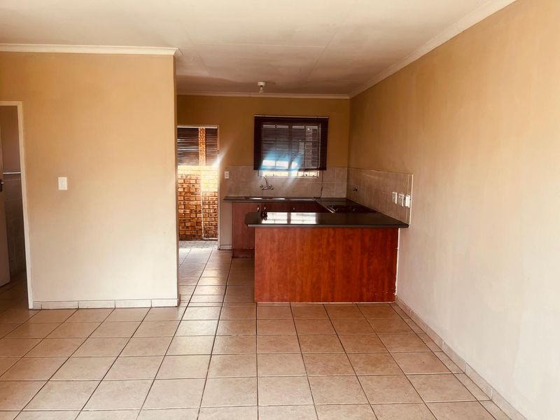 An open-plan living and kitchen area featuring tiled flooring, built-in cabinetry with a laminate countertop, and a functional kitchen layout.