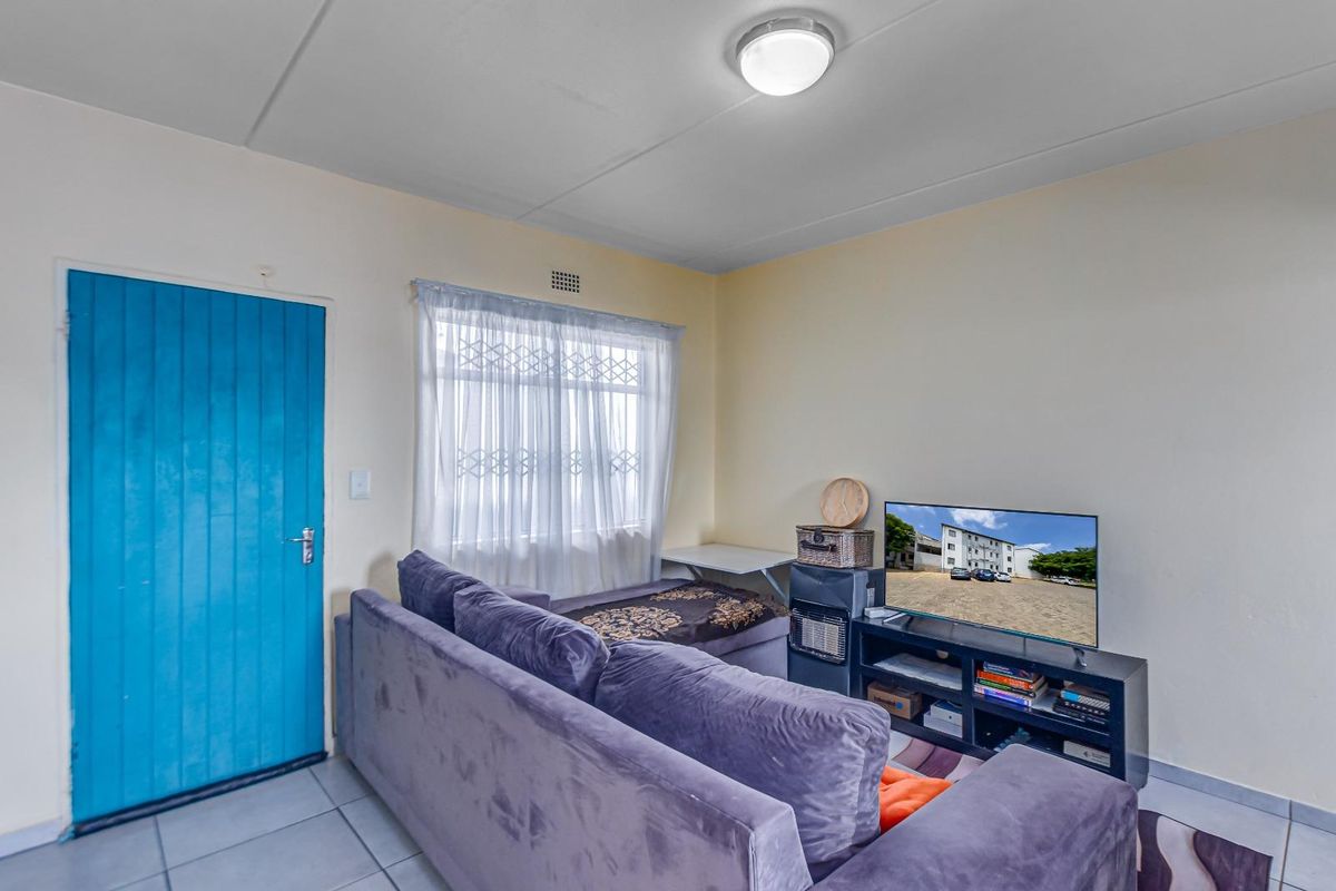 A functional living room featuring tiled flooring, a secure entrance door, and a ceiling-mounted light fixture.