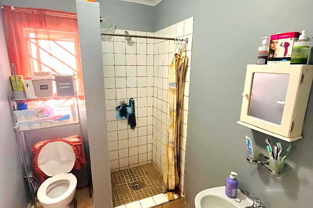 A functional bathroom featuring a tiled shower enclosure, wall-mounted basin, and toilet, with neutral wall paint and tiled flooring throughout.