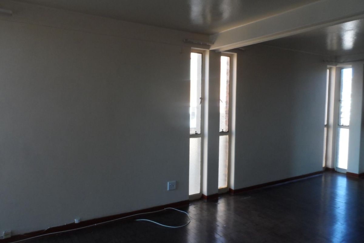 An empty living area featuring dark parquet flooring and tall, narrow windows that provide natural light.