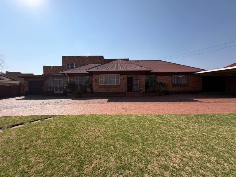 Front elevation of a single-story brick house featuring a large paved driveway, attached carport, and a well-maintained front lawn.
