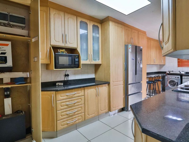 A functional kitchen featuring light wood cabinetry, granite countertops, tiled floors, and integrated laundry facilities, offering a practical layout for daily use.