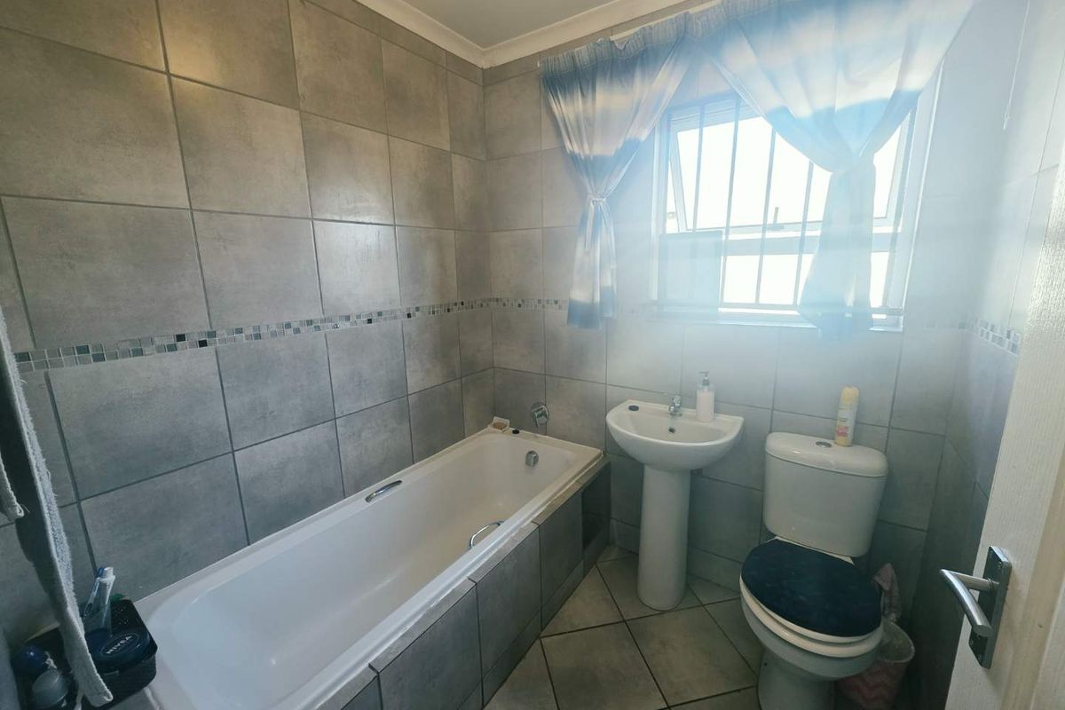 A functional bathroom featuring a built-in bathtub, pedestal basin, and toilet, finished with neutral grey ceramic wall and floor tiles.