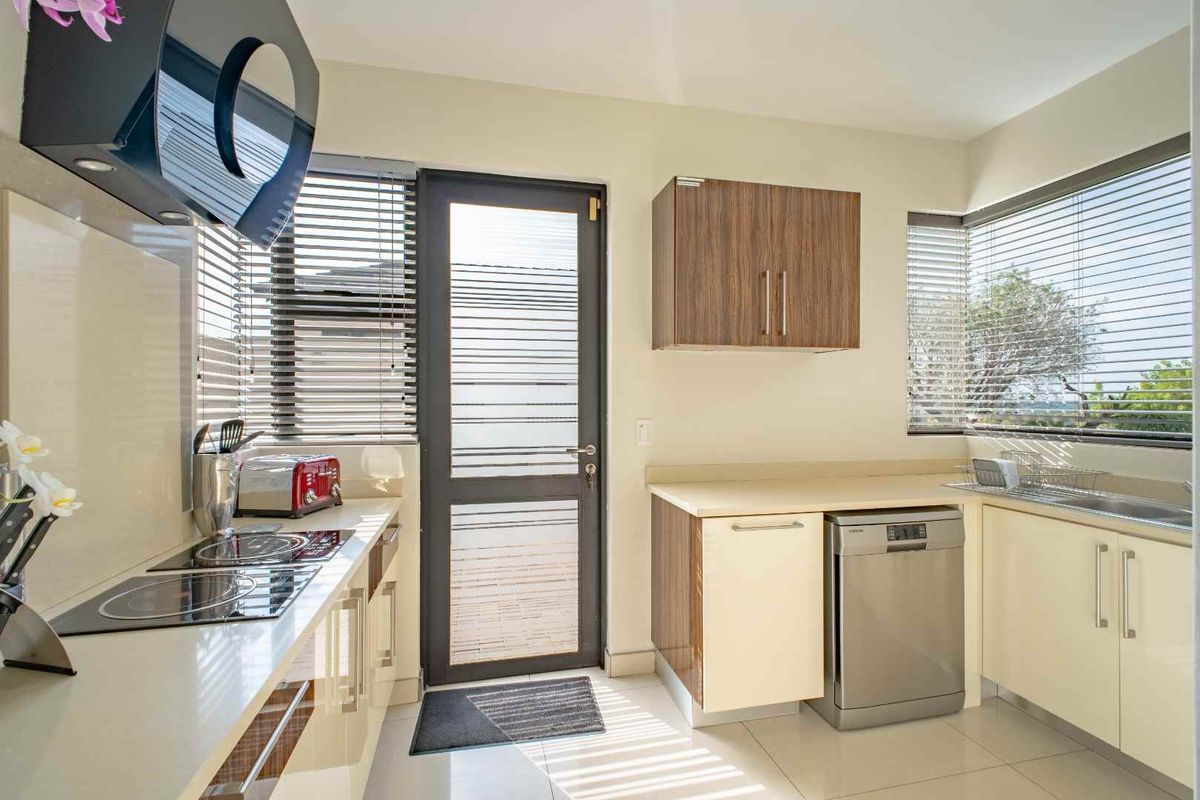 Modern kitchen featuring sleek cabinetry, integrated cooktop, extractor fan, and stainless steel sink with large windows providing ample natural light.
