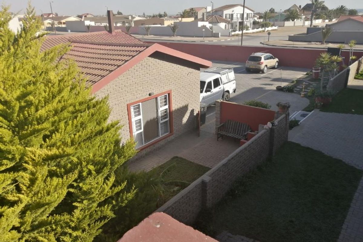 Elevated view of the guest house exterior, featuring brick masonry walls, a pitched roof, paved driveway, and enclosed garden area.
