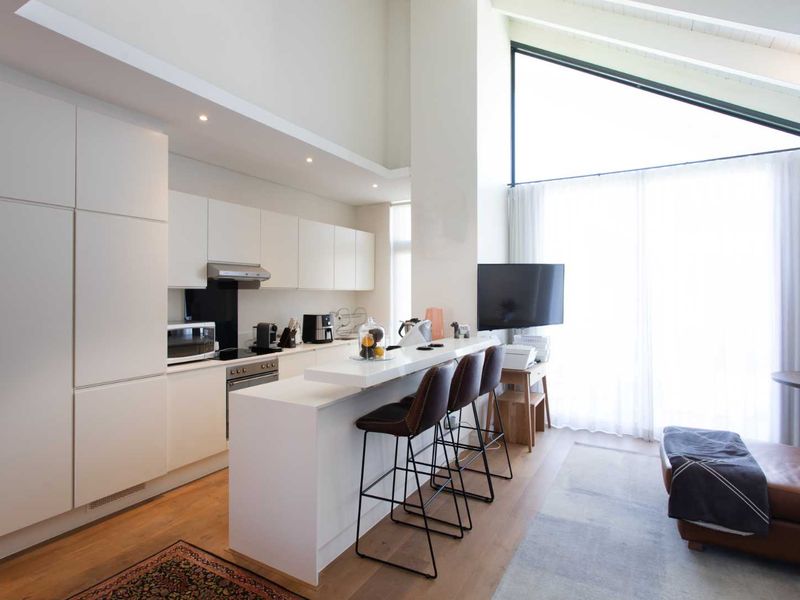 Modern open-plan kitchen featuring sleek white cabinetry, integrated appliances, a breakfast bar, and a striking vaulted ceiling with expansive windows for natural light.