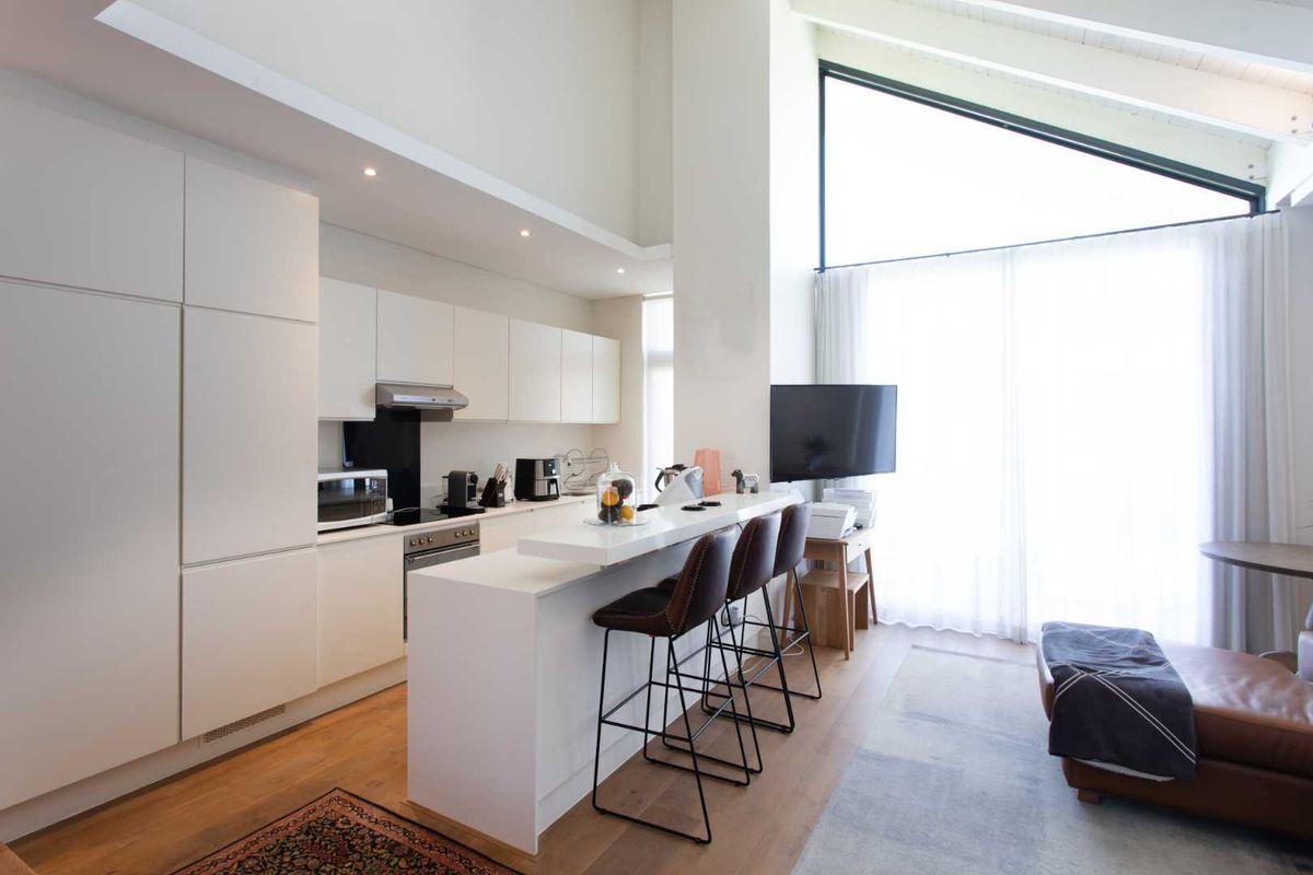 Modern open-plan kitchen featuring sleek white cabinetry, integrated appliances, a breakfast bar, and a striking vaulted ceiling with expansive windows for natural light.