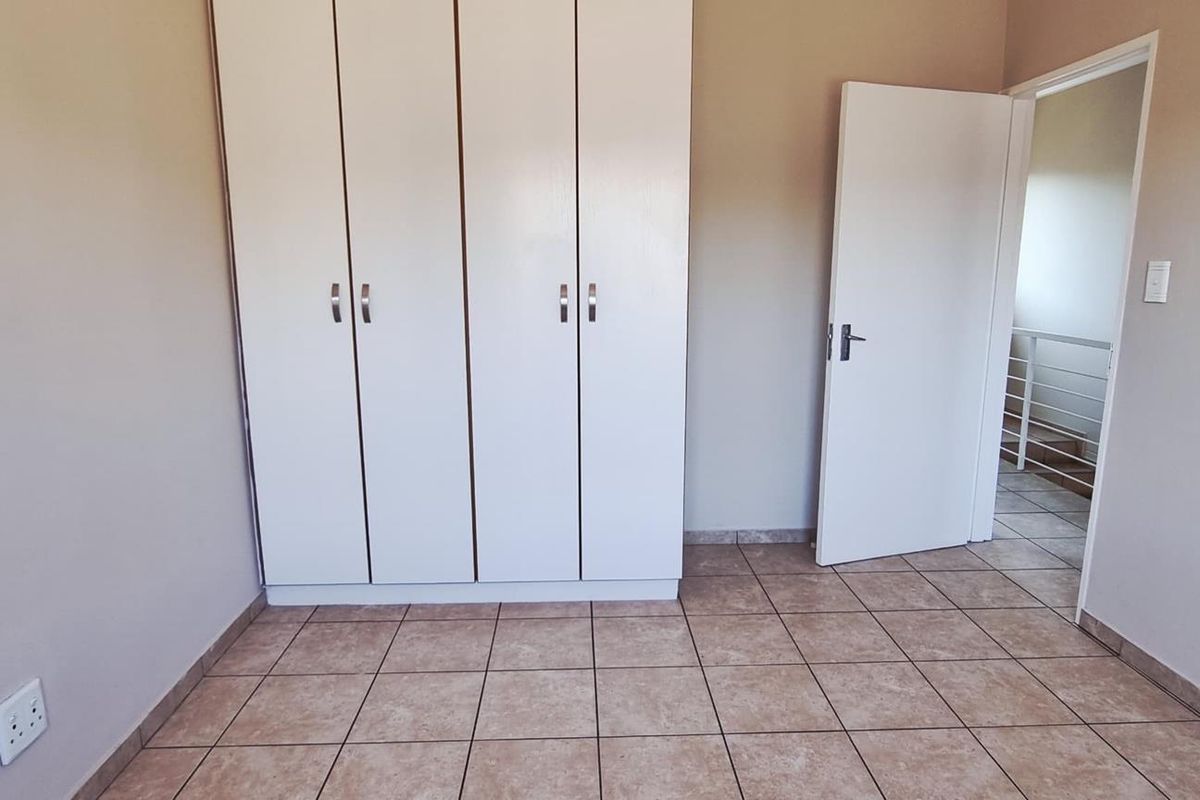 A clean, empty bedroom featuring neutral wall tones, tiled flooring, and built-in cupboards, offering a versatile space ready for personalization.