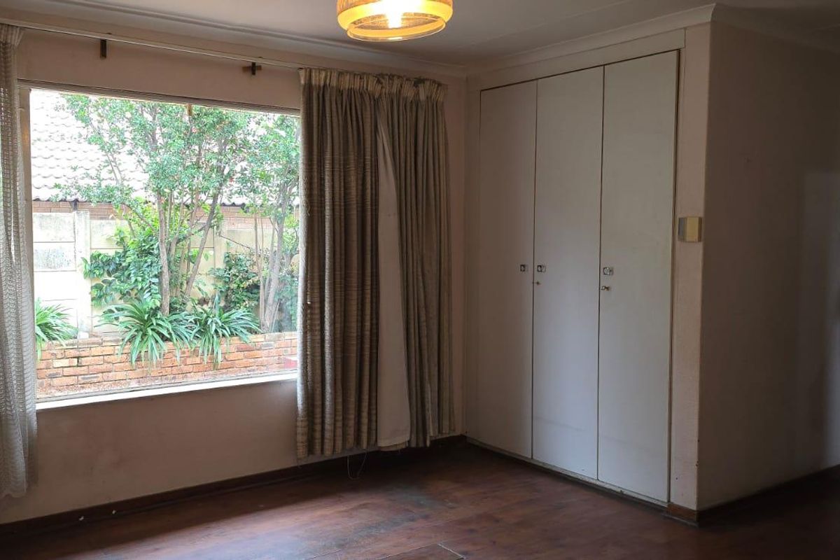 A bedroom featuring built-in cupboards, large window with garden view, and timber-look flooring.
