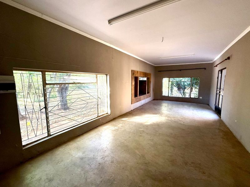 Spacious, empty living area featuring large windows with security bars, concrete flooring, and a built-in wall niche, requiring cosmetic updates.
