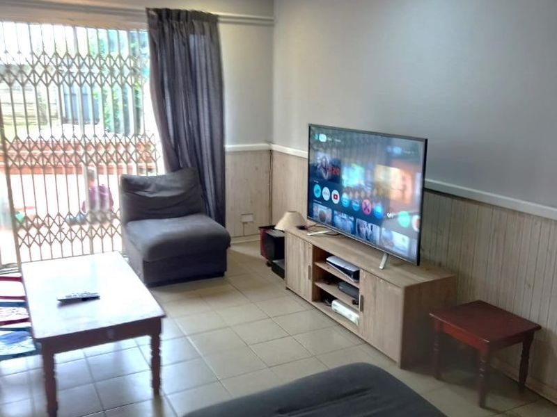 A living room featuring tiled flooring, timber wall paneling, and a timber ceiling with recessed lighting, leading to an exterior security gate.