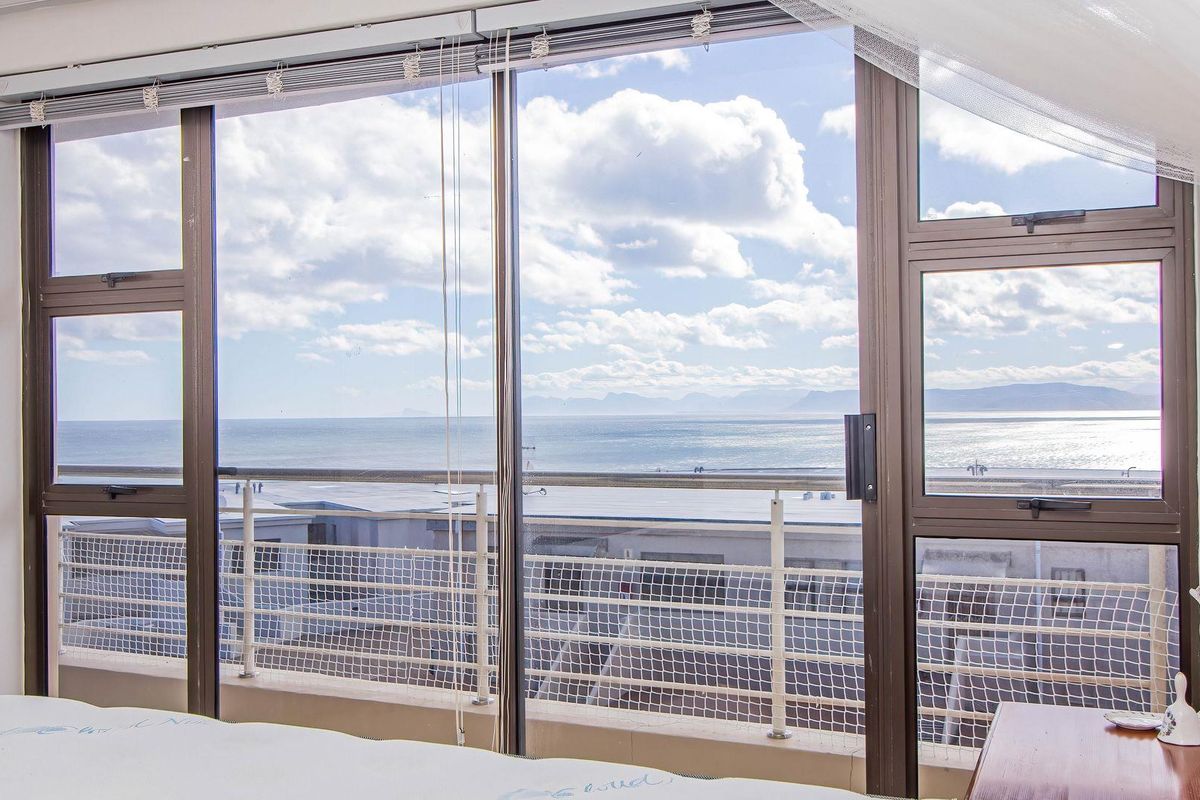 A bedroom featuring large sliding glass doors that open onto a balcony, offering expansive ocean and coastal views.