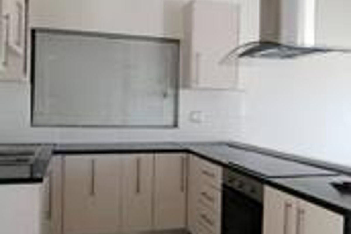 A clean, modern kitchen featuring white cabinetry, dark granite countertops, built-in oven, ceramic hob, and a stainless steel extractor fan.