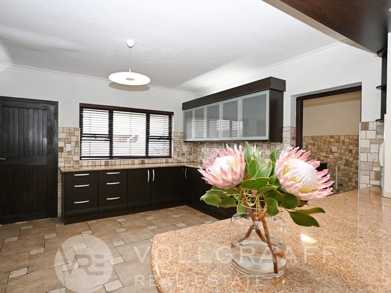 A well-maintained kitchen featuring dark cabinetry, granite countertops, tiled backsplash, and tiled flooring with a functional layout.