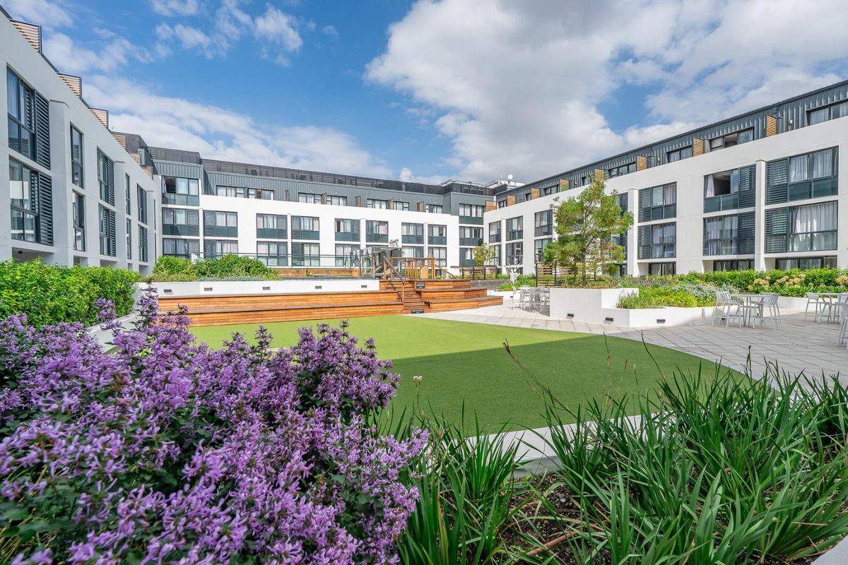 A well-maintained communal courtyard area featuring landscaped gardens, artificial turf, timber decking, and paved seating areas within a modern apartment complex.