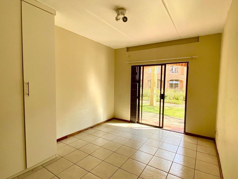A bright, empty bedroom featuring tiled flooring, a built-in wardrobe, and a sliding glass door providing access to the exterior.