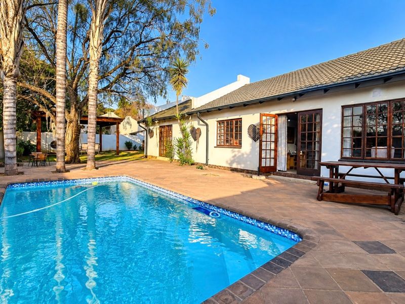 A well-maintained outdoor pool area featuring a tiled patio, swimming pool, and direct access to the home through timber-framed doors.