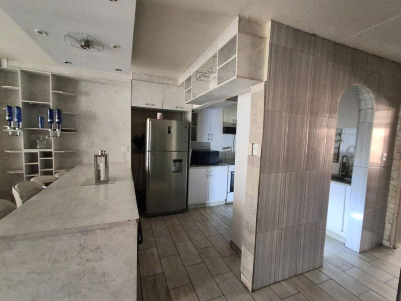 A functional kitchen area featuring built-in cabinetry, stone-look countertops, and tiled flooring, connected to an adjacent space via a decorative archway.