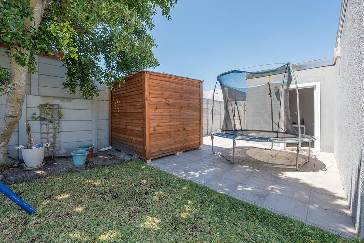 A rear outdoor area featuring a paved patio, a small lawn, and a precast concrete boundary wall.