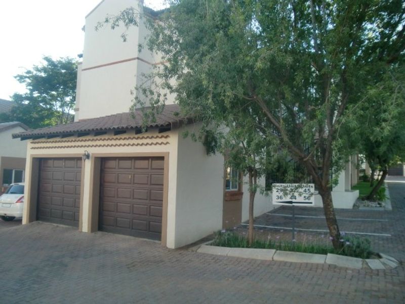 Exterior view of an apartment complex featuring a double garage with tiled roofing and a paved driveway area.