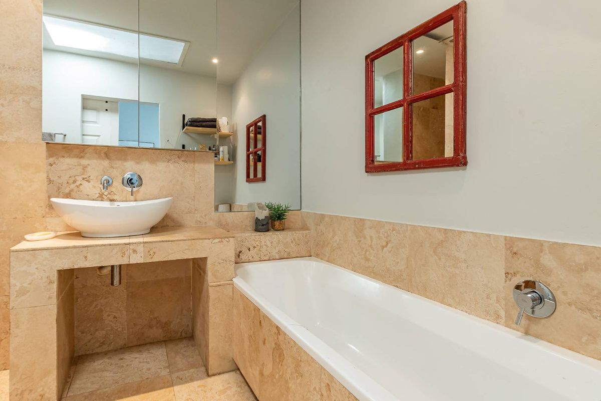 A well-maintained bathroom featuring a stone-tiled vanity with a vessel sink, a built-in bathtub, and a large wall-mounted mirror.