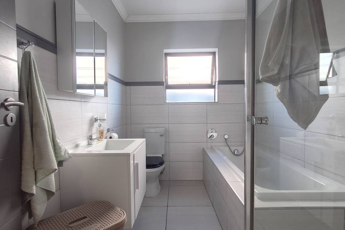 A clean, modern bathroom featuring a built-in bathtub, glass shower enclosure, vanity cabinet with mirror, and tiled walls.