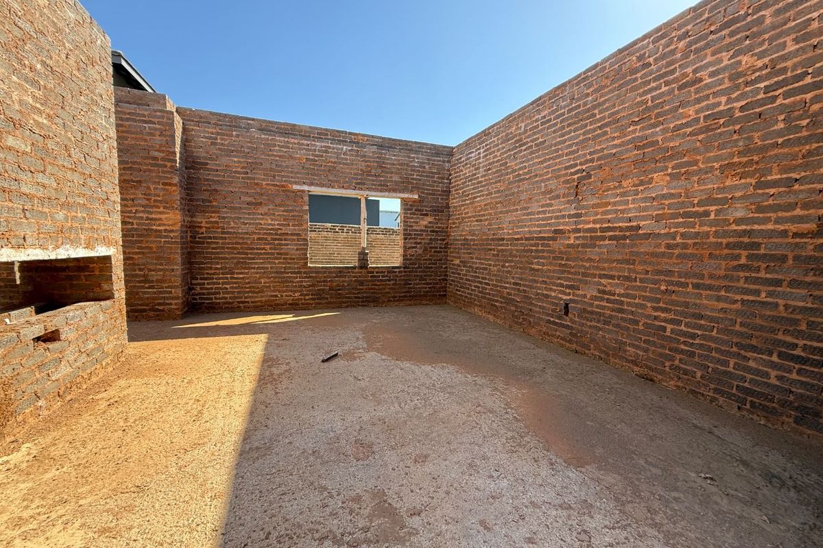 An unfinished room under construction featuring exposed brick walls, a concrete floor, and an open window frame, awaiting final interior finishes.