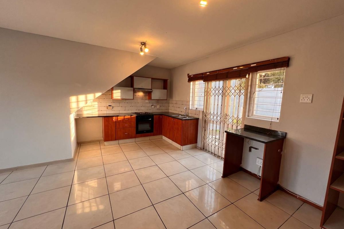 A functional kitchen featuring built-in cabinetry, an oven, hob, extractor fan, and a breakfast counter, with tiled flooring and direct access to the exterior.