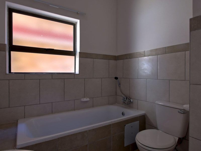 A functional bathroom featuring a built-in bathtub, toilet, and neutral wall tiling, providing a clean and practical space.