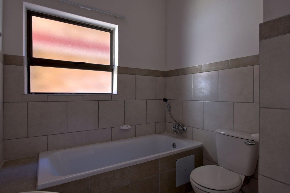 A functional bathroom featuring a built-in bathtub, toilet, and neutral wall tiling, providing a clean and practical space.
