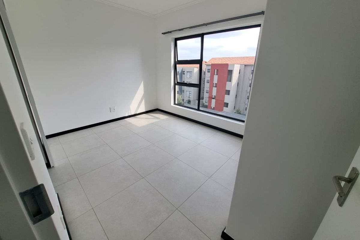 A bright, empty bedroom featuring neutral tiled flooring and large aluminium-framed windows, offering a clean and modern blank canvas.