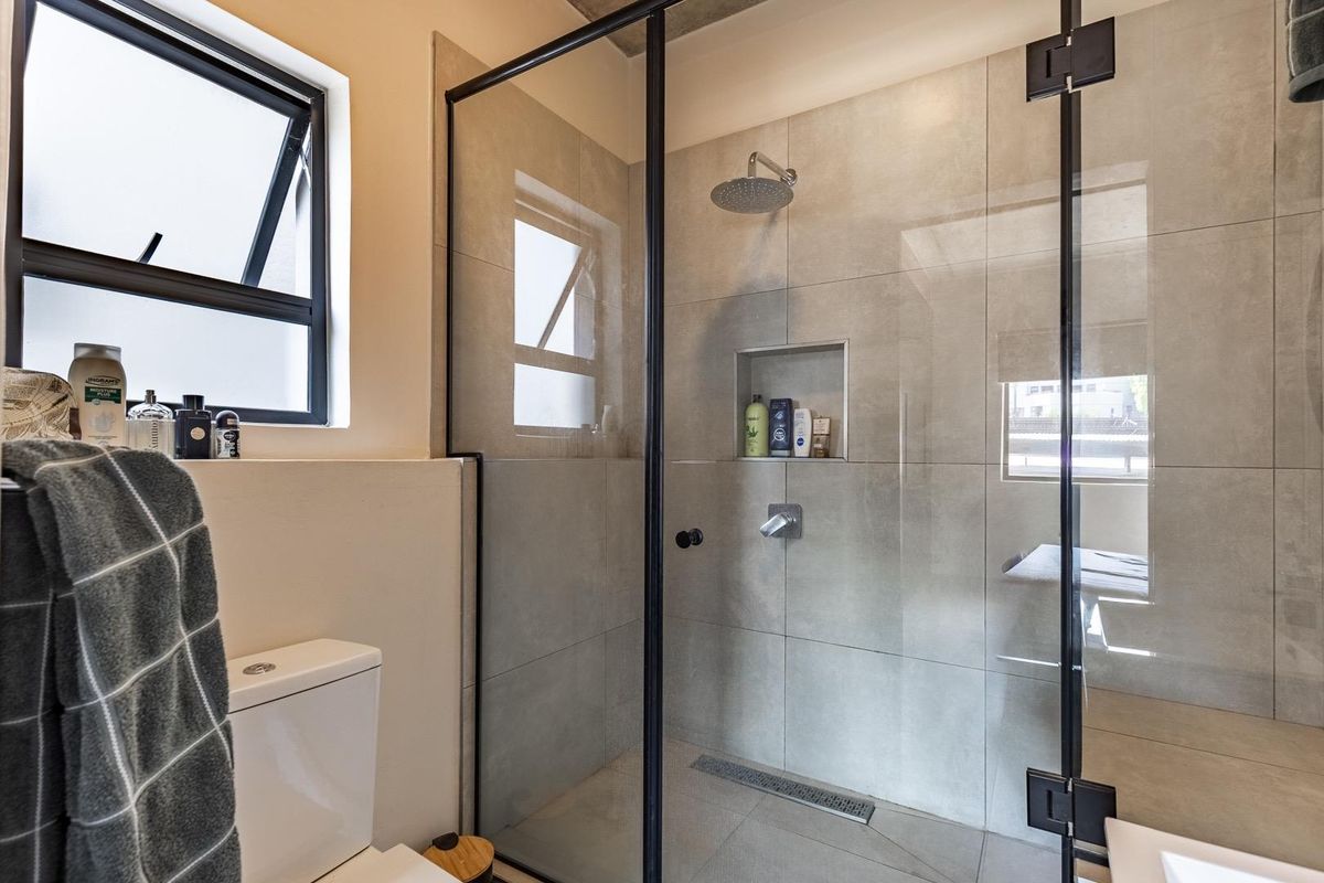 Modern bathroom featuring a walk-in shower with a black-framed glass enclosure, rainfall showerhead, built-in wall niche, and a contemporary toilet.