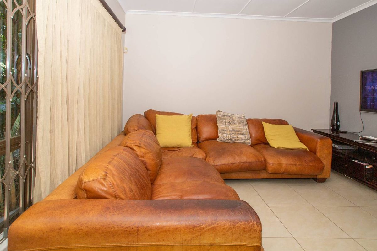 A living room featuring tiled flooring and a sliding door with a security gate, providing access to the exterior.