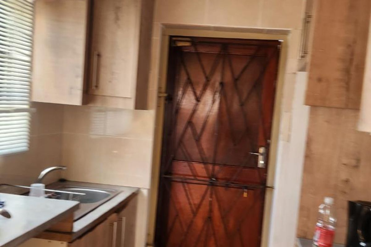 A functional kitchen featuring laminate cabinetry, tiled splashbacks, and a stainless steel sink, with a secure external door access.